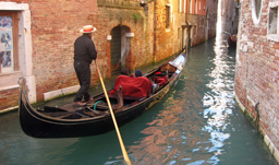 Gondolier along a canal through the houses of Venice - Italy